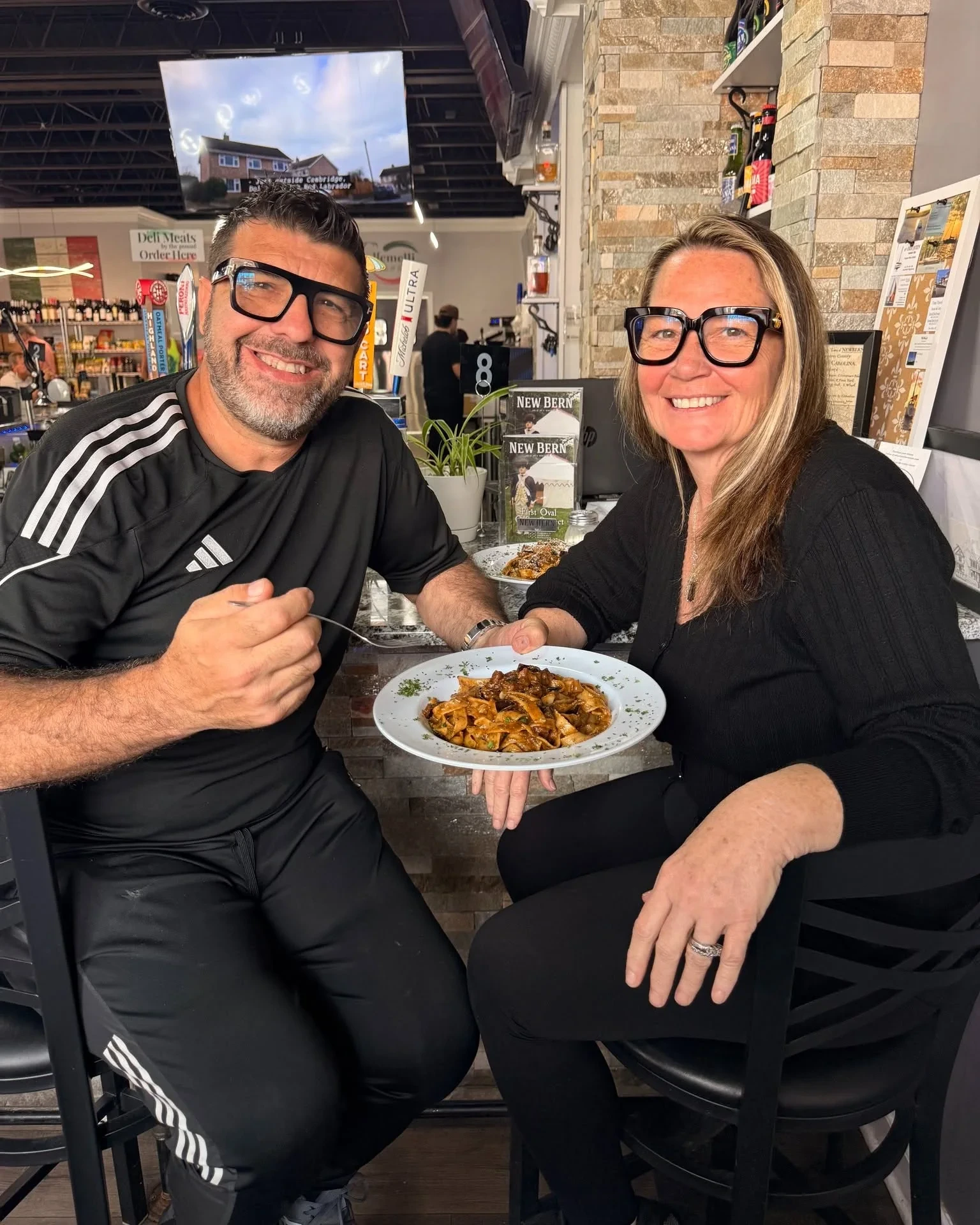 Piero and Paula Passalacqua smiling at the Gemelli counter over a plate of pappardelle