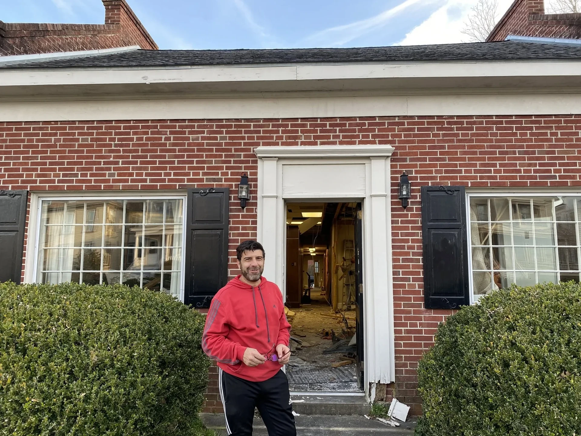 Piero Passalacqua in a red hoodie outside the brick building, its front door open onto a gutted interior at the start of the renovation