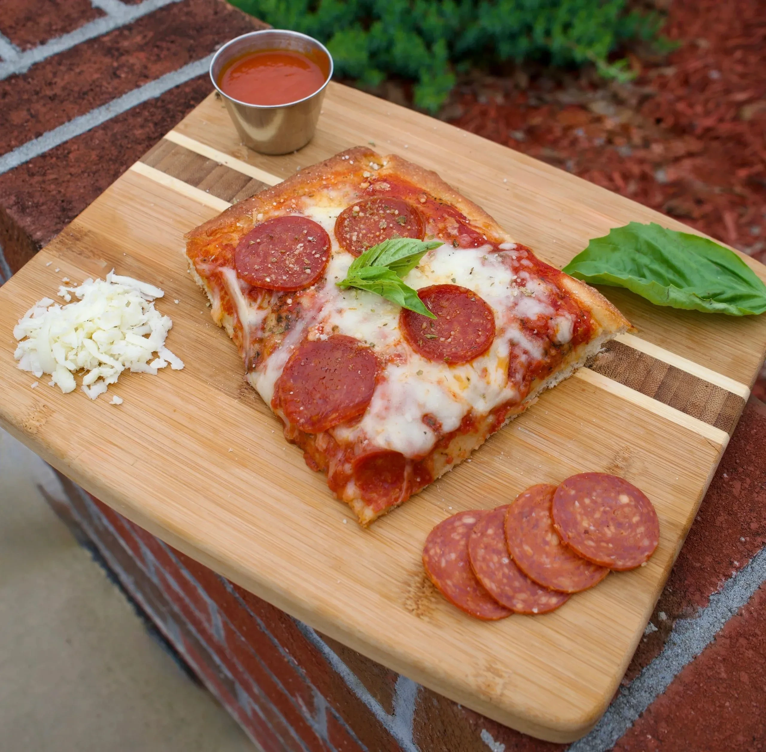 A slice of Gemelli Sicilian pizza with pepperoni, mozzarella and basil